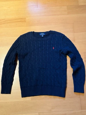 Mörkblå tröja från Polo Ralph Lauren - Mörkblå kabelstickad tröja från Polo Ralph Lauren och röd broderad logga på bröstet. Priser är ej hugget i sten🙌