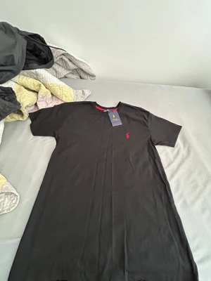 Polo tröja - Snygg svart t-shirt från Polo Ralph Lauren i storlek XL. Klassisk passform med korta ärmar och rund hals. Liten röd logga broderad på bröstet och en diskret röd detalj på insidan av kragen. Tillverkad i mjuk bomull för skön känsla. Snygg säljer för jag behöver pengar helt nytt det står Xl men det är S