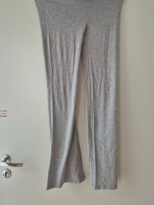 Grå  leggings med utsvängda ben - Säljer ett par ljusgrå yoga byxor från Gina och utsvängda ben. De är mjuka och stretchiga, perfekta för en chill och avslappnad stil. Materialet känns som bomull eller en bomullsblandning. Passformen är tight upptill och släpper vid benen. Storlek 158/164. 