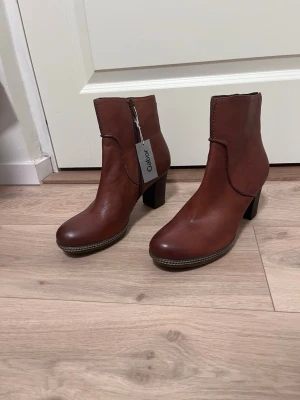 Bruna skinnpumps med klack från Gabor - Snygga bruna pumps i skinn från Gabor med markerad klack och rundad tå. Skorna har dekorativa sömmar och dragkedja på insidan för enkel påtagning. Perfekta för dig som vill ha en stilren och klassisk look. Lappen kvar.