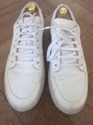 Vita låga sneakers i läder - Stilrena vita sneakers i lågt snitt med klassisk design och vita skosnören. Tillverkade i slätt läder med diskreta sömmar och vit sula. Perfekta för en clean och enkel look. Äkta köpt på Vestaire 