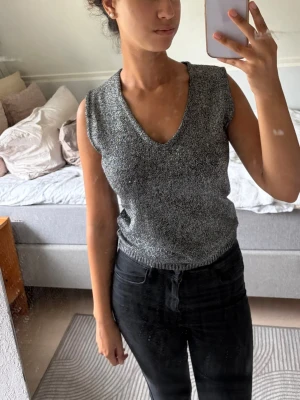 Glittrig silver topp - Säljer en glittrig silverfärgad topp med v-ringning och ärmlös design. Perfekt för fest eller när man vill klä upp sig lite extra!🪩