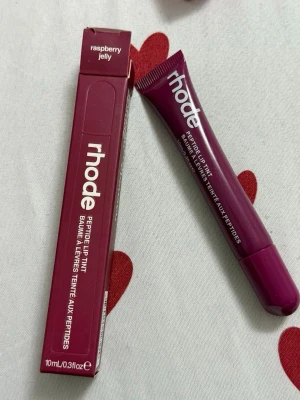 rhode Peptide Lip Tint Raspberry Jelly - Läppbalsam från rhode i färgen Raspberry Jelly. Tuben är mörklila med vit text och rymmer 10 ml. Ger en lätt tonad finish och innehåller peptider för extra vård. Perfekt för dig som vill ha både färg och fukt till läpparna.