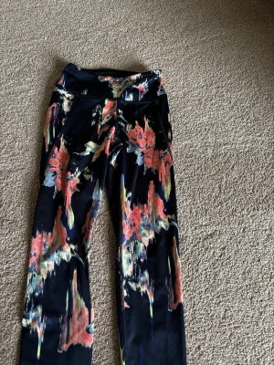 Mönstrade leggings från H&M Sport XS - Säljer ett par snygga leggings från H&M Sport i storlek XS. De är svarta med färgstarkt abstrakt mönster i rött, orange, blått och gult. Stretchigt material som sitter skönt och passar perfekt till träning eller chill. Hög midja för extra komfort.