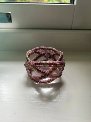 Rosa och guldigt pärlarmband - Unikt armband med flera lager av små rosa och guldfärgade pärlor i korsande mönster. Armbandet är flexibelt och har en bohemisk vibe, perfekt för att addera färg till din outfit. Materialet består av plast- och metallpärlor i olika former och storlekar. Köpt utomlands💗