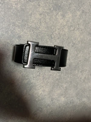Vändbart vitt och svart skärp med H-spänne - Stilrent vändbart skärp i vitt och svart skinn med ett stort, silverfärgat H-format spänne. Perfekt accessoar för att lyfta din outfit med en lyxig touch och enkel att matcha tack vare de klassiska färgerna.