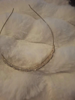 Glittrigt tiara med strassdetaljer - Säljer ett elegant tiara i metall med gnistrande strass i ett kronliknande mönster. Diademet är silvrigt och har en tunn, smidig form som sitter bekvämt på huvudet. Perfekt för att ge din look extra bling och princess vibes.