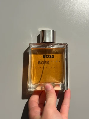BOSS Bottled parfym - Stilren parfymflaska från BOSS med rektangulär form och silverfärgat lock. Flaskan är genomskinlig och innehåller en gyllene vätska. Perfekt för dig som gillar klassiska och eleganta dofter.