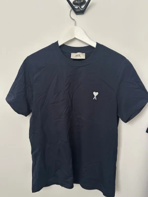 Mörkblå t-shirt från Ami - Snygg mörkblå t-shirt från Ami Alexandre Mattiussi med liten vit logga med hjärta och bokstaven A på bröstet. Klassisk rund hals och korta ärmar. Tillverkad i mjuk bomull som känns skön mot huden.