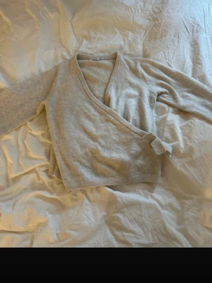 Beige omlottkofta i mjuk stickad kvalitet - Superfin beige omlottkofta i mjuk stickad kvalitet med långa ärmar och knytband i sidan. Perfekt för lager-på-lager och enkel att styla till olika outfits. Koftan har ribbade muddar och en klassisk v-ringning.