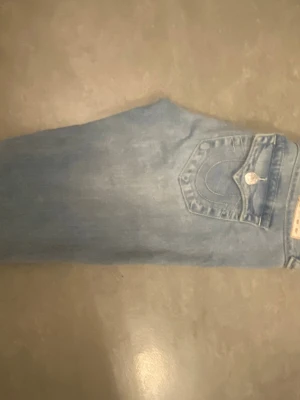Ljusblå bootcut jeans med fickdetaljer - Säljer ett par ljusblå bootcut jeans med snygga fickdetaljer och knappar bak. Jeansen har klassisk femficksmodell och är tillverkade i denim. Perfekta för dig som gillar retrovibbar och vill ha ett par jeans med lite vidare ben.