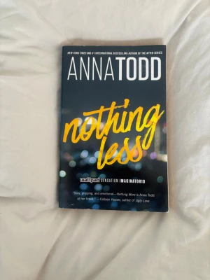 Nothing Less av Anna Todd - En ungdomsroman av Anna Todd med titeln 'Nothing Less'. Omslaget är svart med gul och vit text och har en suddig stadssilhuett i bakgrunden. Boken är i pocketformat och tryckt på papper. Perfekt för dig som gillar romantik och drama.