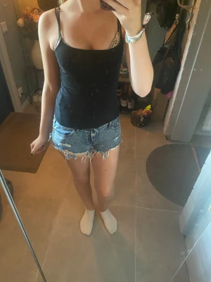Blå jeansshorts med fransar - Säljer ett par klassiska blå jeansshorts med råa, fransiga kanter och femficksmodell. Shortsen har normal passform och är tillverkade i bomull. Perfekta för sommaren och ger en avslappnad look.