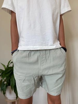 Ljusgröna loose shorts i linne - Säljer ett par ljusgröna shorts i loose passform med elastisk midja och knappstängning. Shortsen har sidofickor och är tillverkade i ett svalt linnematerial, perfekta för varma dagar.