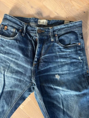 Blå slitna jeans med vintage-look - Säljer ett par jättefina  blå Jack & Jones jeans med tydlig vintage-look och slitningar. Perfekta för dig som gillar en avslappnad och trendig stil. Mått: Midja 39, innerben 75, ytterben 100. 