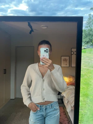 Beige ribbad kofta med knappar - Snygg beige kofta med ribbad struktur och v-ringning. Koftan har tre stora knappar framtill, långa ärmar och en croppad passform. Perfekt att slänga över en topp för en avslappnad look. Nästan aldrig använd. Skriv om ni har nån fråga!!🩷🫶🏼