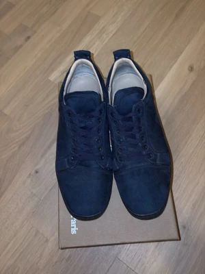 Mörkblåa låga sneakers i tyg - Snygga mörkblå sneakers i tyg med klassisk låg profil och matchande mörkblå snörning. Skorna har en röd detalj på yttersulan och vit insida. Perfekta för en avslappnad och stilren look.
