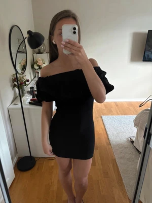 Svart offshoulder kort klänning - Säljer en svart kort klänning med offshoulder-design och volang upptill. Klänningen har en tight passform och är ärmlös, vilket ger en trendig och ungdomlig look. Perfekt för dig som vill sticka ut med en enkel men snygg outfit.Passar xs