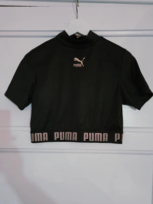 Puma svart crop top st L - Svart crop top från Puma med kort ärm och hög krage. Toppen har en dragkedja framtill och en resårkant nedtill. Toppennär använd 2 gånger. Ej retur.