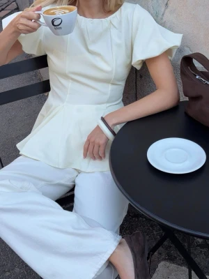 Vit blus med volang och kort ärm - Säljer en söt vit blus med volang nertill och korta, puffiga ärmar. Blusen har en figurnära passform upptill och en lätt utsvängd nederdel som ger en feminin siluett💕💕 skicka gärna prisförslag!!