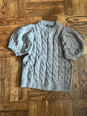 Grå kabelstickad tröja med puffärm - Supersnygg grå stickad tröja med kabelstickat mönster och puffiga korta ärmar. Perfekt för dig som vill ha en mysig men trendig look. Materialet känns mjukt och gosigt. Använd endast 2 gånger❣️❣️
