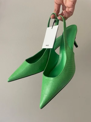 Gröna pumps med ormmönster från MNG - Snygga gröna pumps från MNG med spetsig tå och slingback-rem. Skorna har ett trendigt ormmönster i konstläder och smal klack som ger en cool och modern vibe. Aldrig använda, prislapp kvar! 