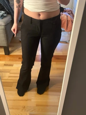 Svarta kostymbyxor bootcut - Säljer ett par svarta kostymbyxor med bootcut-modell och låg midja. Byxorna har hällor för skärp och klassisk knapp- och dragkedjestängning. Perfekta för en clean och stilren look. Fickor baktil