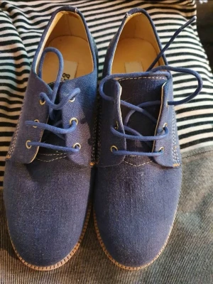 Gram Washed Navy Linen, stl 37 - Säljer ett par blåa loafers i tyg med snörning och kontrastsömmar. Skorna har en klassisk rundad tå och ljus innersula. Perfekta för dig som gillar en enkel men stilren look. Passar storlek 37. Knappt använda 