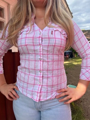 Levi’s Pink Plaid Shirt – Size L (Fits Like M) 💕 - Super cute and timeless Levi’s plaid shirt in excellent condition. Features a flattering fitted silhouette, beautiful pink check pattern, and stylish 3/4 sleeves. Size L, but fits more like a Medium for a tailored look. Perfect for layering or wearing on its own all year round.  ✨ Brand: Levi’s 📏 Size: L (fits like M) 💗 Color: Pink plaid/checkered 👚 Fitted style 🩷 3/4 sleeves ✔️ Excellent condition 📦 Fast shipping 