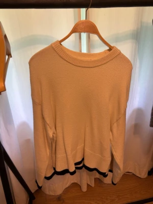 Beige stickad tröja Gina Tricot - Beige stickad tröja från Gina Tricot med rund halsringning och ribbade muddar. Tröjan har svarta ränder längst ner vid fållen och ärmarna, vilket ger en snygg kontrast. Perfekt för lager på lager och enkel att matcha.