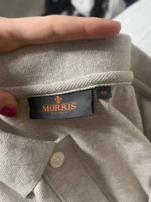Beige piké från Morris - Snygg beige pikétröja från Morris Stockholm i storlek XS. Skjortan har klassisk krage, korta ärmar och knappar framtill. Perfekt för en clean och stilren look. Materialet känns mjukt och bekvämt mot huden.
