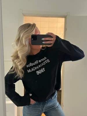 Svart sweatshirt Acne Studios - Säljer en svart sweatshirt Acne Studios med vit text 'Acne Studios Stockholm 1996' på bröstet. Tröjan har en avslappnad passform, rund halsringning och långa ärmar. Perfekt till jeans för en cool och enkel look. Obs ej äkta 