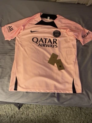 Rosa PSG matchtröja från Nike - Snygg rosa PSG matchtröja med svarta detaljer och Qatar Airways-tryck på bröstet. Tröjan har klubbmärke på vänster sida och Nike-logga på höger. Tillverkad i lätt och ventilerande material, perfekt för träning eller match. Tröjan har storlek L men kan passa M också. Måtten är 71cm lång och bredd 51cm. Finns även shorts till om man vill men då höjs priset 