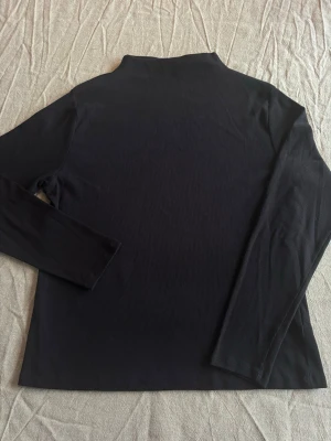 Svart ribbad polotopp - Säljer en svart ribbad halv polotopp med lång ärm. Perfekt basplagg till garderoben och enkel att styla med olika outfits. Tunn stickad kvalitet och klassisk passform.