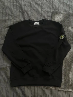 Stone Island tröja🚨Helt ny🚨 - Säljer en helt ny svart långarmad Medium tröja från Stone Island med den klassiska loggan på vänster ärm. Tröjan har rund halsringning, ribbade muddar vid ärmslut och nederkant samt en clean och stilren look. Perfekt för dig som gillar streetwear och vill ha något enkelt men ändå ikoniskt.