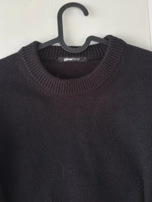 Svart stickad tröja från Gina Tricot - En enkel och stilren svart stickad tröja från Gina Tricot. Tröjan har rund halsringning med ribbstickade detaljer och långa ärmar. Perfekt basplagg att matcha med allt i garderoben.