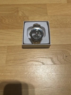 Silverfärgad Subaru klocka med länk - Snygg klocka från Subaru med silverfärgat metallarmband och rund urtavla. Klockan har svarta och blå detaljer runt urtavlan, samt flera mindre urtavlor inuti. Perfekt för dig som gillar en sportig och stilren accessoar.