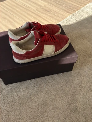 Valentino flycrew - Snygga valentino flycrews i rött och vitt med ovandel i mocka och detaljer i läder. Skorna har röda skosnören och vit sula. Skadade bak i hälen och har tappat 4 nitar 