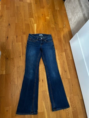 Mörkblå bootcut jeans - Säljer ett par mörkblå bootcut jeans med klassisk femficksdesign och kontrastsömmar. Jeansen har utsvängda ben och fickor med lock och knapp bak. Perfekta för en avslappnad men ändå trendig look.