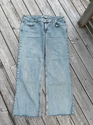Ljusblåa raka jeans med rå kant - Säljer ett par ljusblå jeans med rak passform och rå, fransig kant nedtill. Jeansen har klassisk femficksdesign och hög midja. Perfekta för en avslappnad och trendig look. Materialet är denim i bomull.