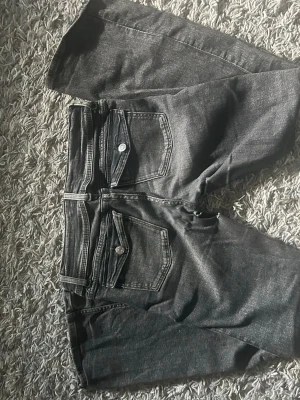 Grå bootcut jeans  - Säljer ett par grå jeans med bootcut-modell och snygga ficklock med knapp framtill. Jeansen har klassisk femficksdesign och är gjorda i ett mjukt denimtyg med lite stretch. Perfekta för dig som gillar en avslappnad men trendig look. Som visat på bild 4 och 5 så är de hål i inre låren därav lägre pris!! Storlek 158 från gina tricot.