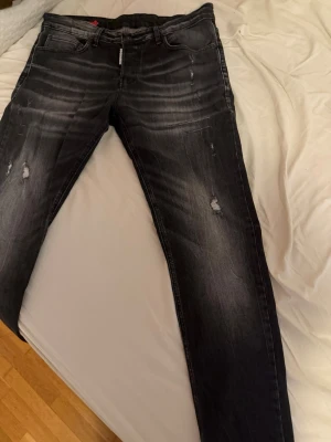 Svarta slitna jeans från Dsquared2 - Snygga svarta jeans från Dsquared2 med slitningar och lätt tvättad look. Jeansen har smal passform, klassiska fem fickor och detaljerade slitningar på benen för en trendig vibe. Perfekta för dig som gillar streetstyle och vill sticka ut.