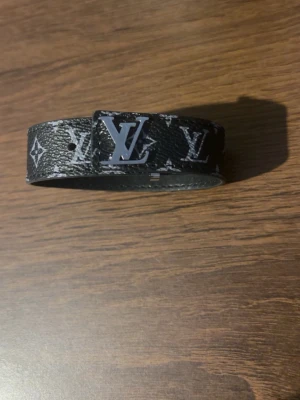 Armband - Snyggt svart armband med klassiskt monogrammönster i vitt och silverfärgat spänne. Bältet är tillverkat i skinn och har en stilren, modern look som passar till många outfits.