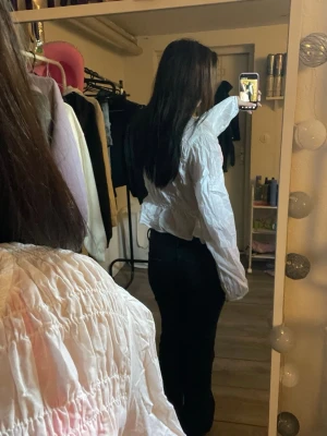 Vit smockad blus med volang - Säljer en vit blus med smockad överdel och volang nedtill. Blusen har långa ärmar och en lätt rynkad struktur som ger en söt och trendig look. Perfekt att styla med jeans eller kjol för en fräsch outfit.💕