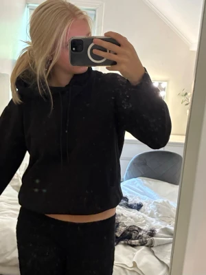 Svart hoodie med huva och magficka - En enkel svart hoodie med huva och dragsnören. Hoodien har en klassisk magficka framtill och ribbade muddar vid ärmslut och nederkant. Perfekt för en chill och avslappnad stil. Materialet ser ut att vara mjukt och bekvämt, troligen bomullsblandning.