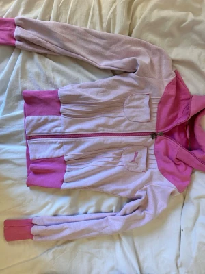 Ljusrosa hoodie från Puma - Säljer en ljusrosa hoodie från Puma med dragkedja framtill och ribbade muddar i mörkare rosa. Två fickor framtill med dekorativa sömmar och Puma-logga broderad på ena fickan. Hoodien har en sportig look och är gjord i mjukt bomullsmaterial.