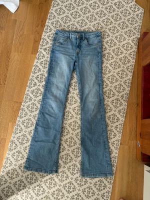 Blå bootcut jeans från Kappahl - Snygga ljusblå bootcut jeans från Kappahl i storlek 158. Jeansen har klassisk femficksmodell, normalhög midja och utsvängda ben. Tillverkade i mjukt stretchigt denimtyg med lätt slitningar för en avslappnad look. Har används ett fåtal gånger men säljer pga inte min stil