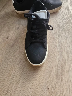 Svarta Jack & Jones sneakers - Svarta sneakers från Jack & Jones med vita detaljer på häl och plös. Skorna har klassisk låg profil, svarta skosnören och vit sula. Tillverkade i syntetmaterial med stilren design som passar till många outfits.