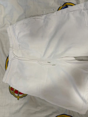 Vita shorts med snörning från Pull&Bear - Säljer ett par vita shorts från Pull&Bear med snörning i midjan. De har en avslappnad passform och är tillverkade i mjukt bomullsmaterial, perfekta för varma dagar. Klassisk design utan mönster eller extra detaljer.