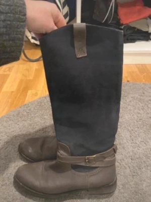 Gant stövlar - Säljer ett par höga stövlar mockaskaft. Stövlarna har en dekorativ rem med spänne runt ankeln och dragkedja på sidan för enkel på- och avtagning. Perfekta för att ge din outfit en snygg touch. De är välanvända ( se bilder) 
